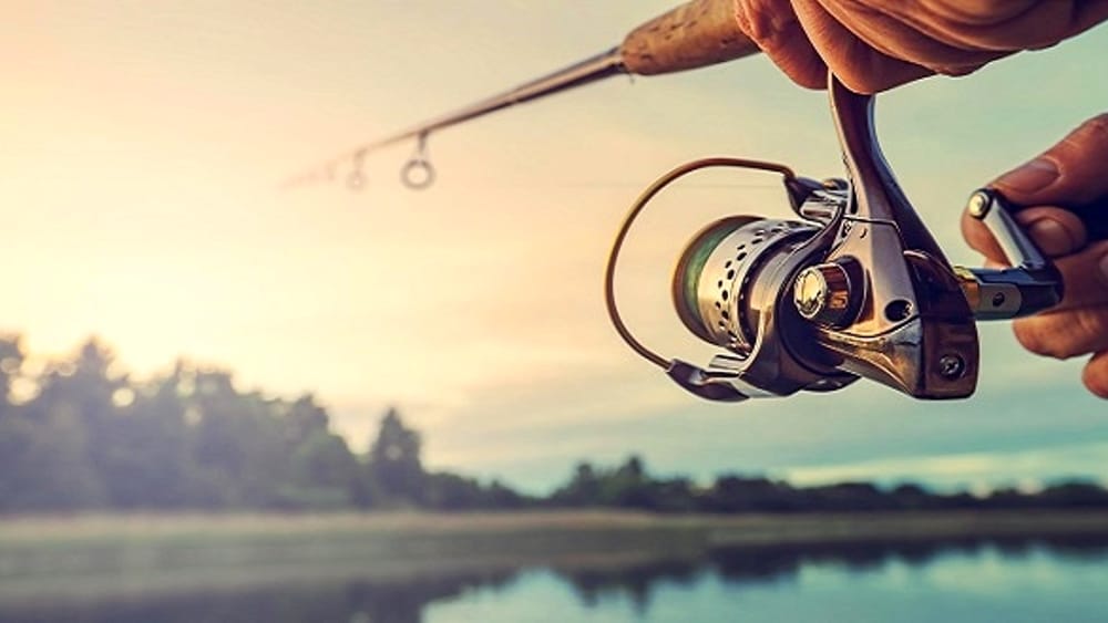 Mano con la canna da pesca che lancia l'amo nel lago